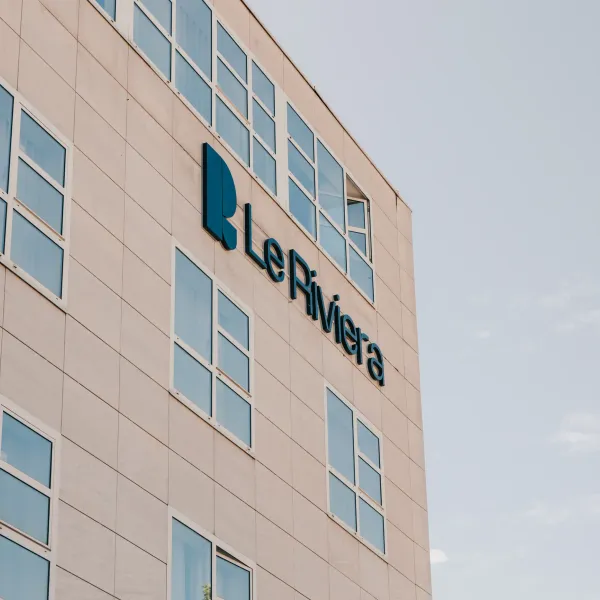 Bâtiment beige avec des fenêtres rectangulaires affichant le logo et le nom "Le Riviera" en bleu