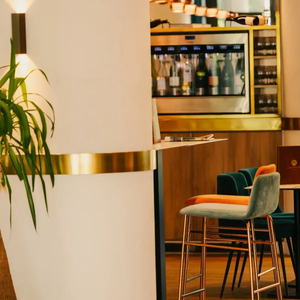 Un intérieur de restaurant avec des tables, des chaises et un bar visible en arrière-plan, éclairé par des lumières murales