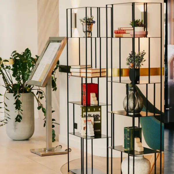 Étagère noire avec divers objets décoratifs, dont des livres, des vases et des plantes, dans un espace intérieur moderne