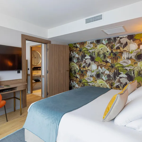 Chambre d'hôtel avec un lit, une chaise orange, un bureau avec un ordinateur portable, une télévision et une porte ouverte sur une salle de bain