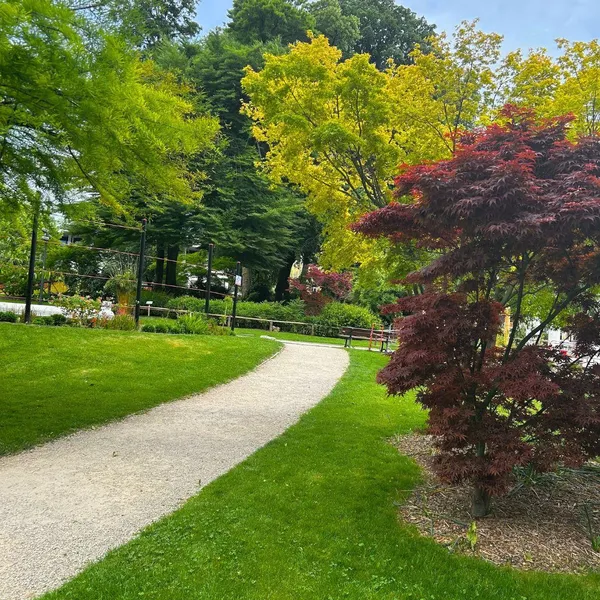 Un sentier de gravier sinueux traverse un parc arboré avec des arbres aux feuilles vertes, jaunes et rouges