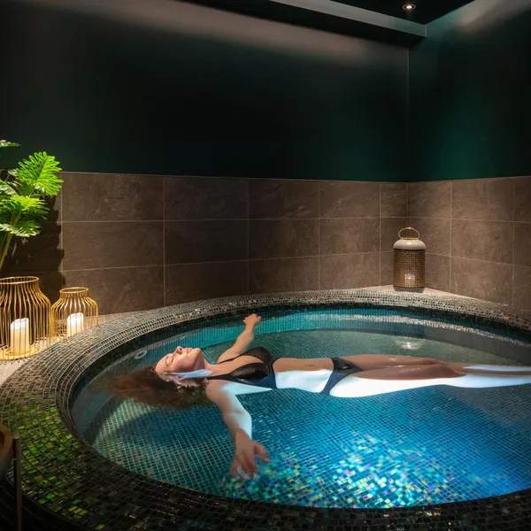 Une personne allongée dans un bain à remous circulaire entouré de bougies et de plantes vertes