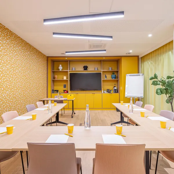 Salle de réunion avec tables, chaises, écran, tableau blanc, décoration murale et plantes