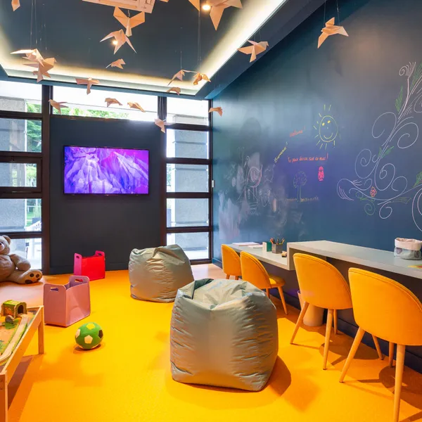 Salle de jeux colorée avec des poufs, un tableau noir décoré, un écran mural et des jouets sur une table basse