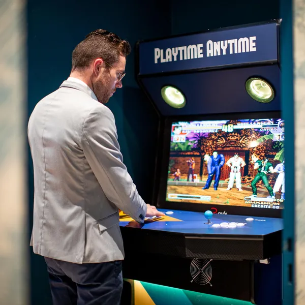 Un homme en costume joue à un jeu vidéo de combat sur une borne d'arcade