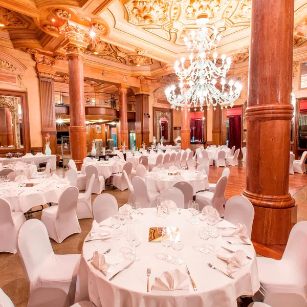Salle de réception luxueuse avec tables rondes couvertes de nappes blanches, chaises assorties et lustres suspendus au plafond orné