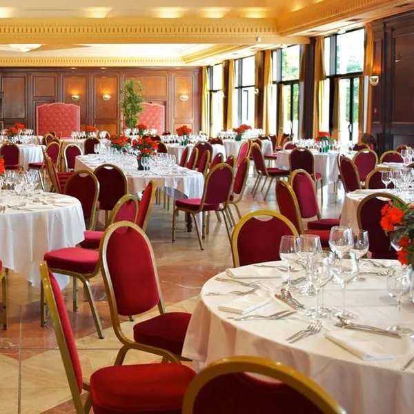 Salle de réception avec tables rondes couvertes de nappes blanches, des chaises rouges et des fleurs rouges en centre de table