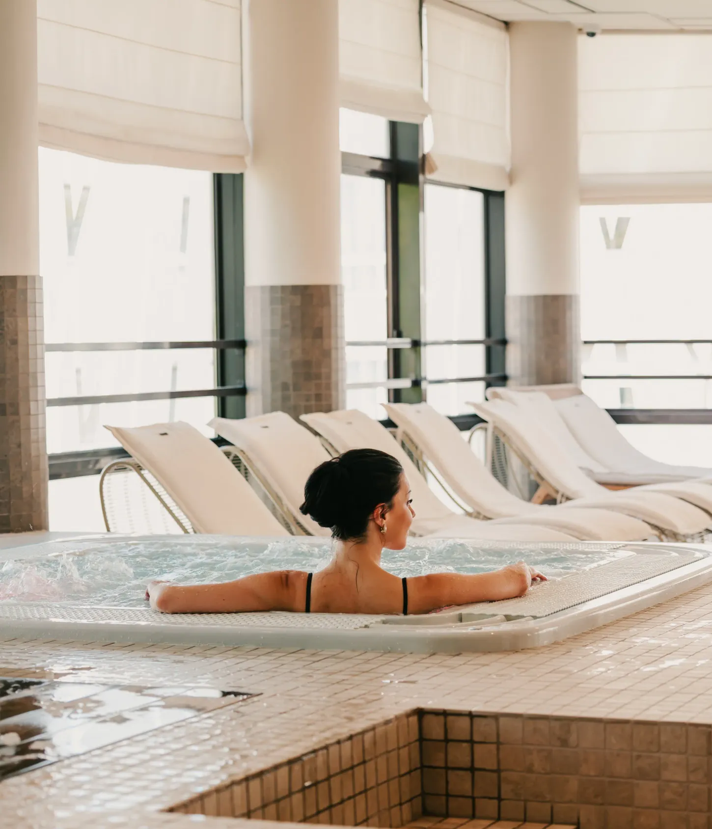 Eine Frau liegt in einem Innen-Whirlpool mit Liegestühlen im Hintergrund.