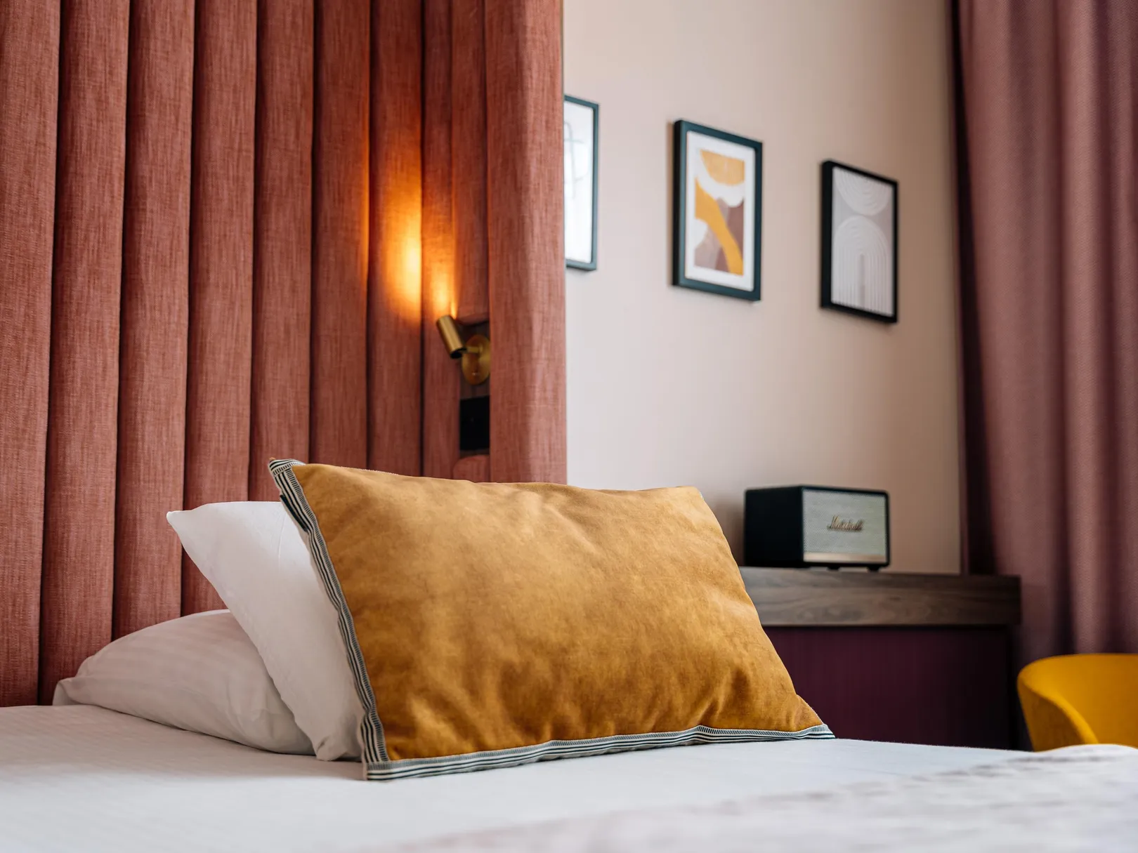 Bed with pillows, a lit lamp and frames on the wall