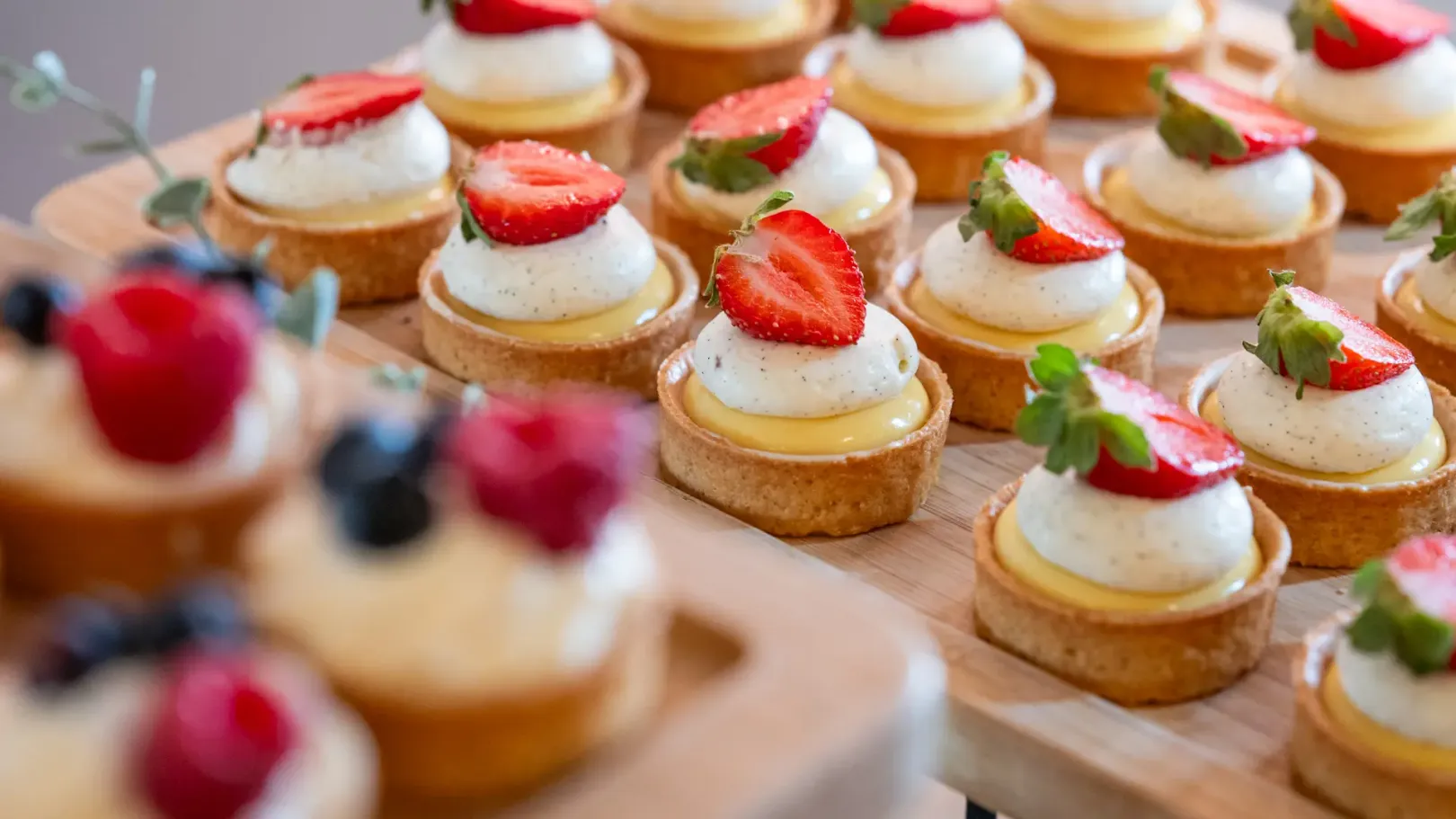 Petits gâteaux ronds garnis de crème et de fraises sur une planche en bois