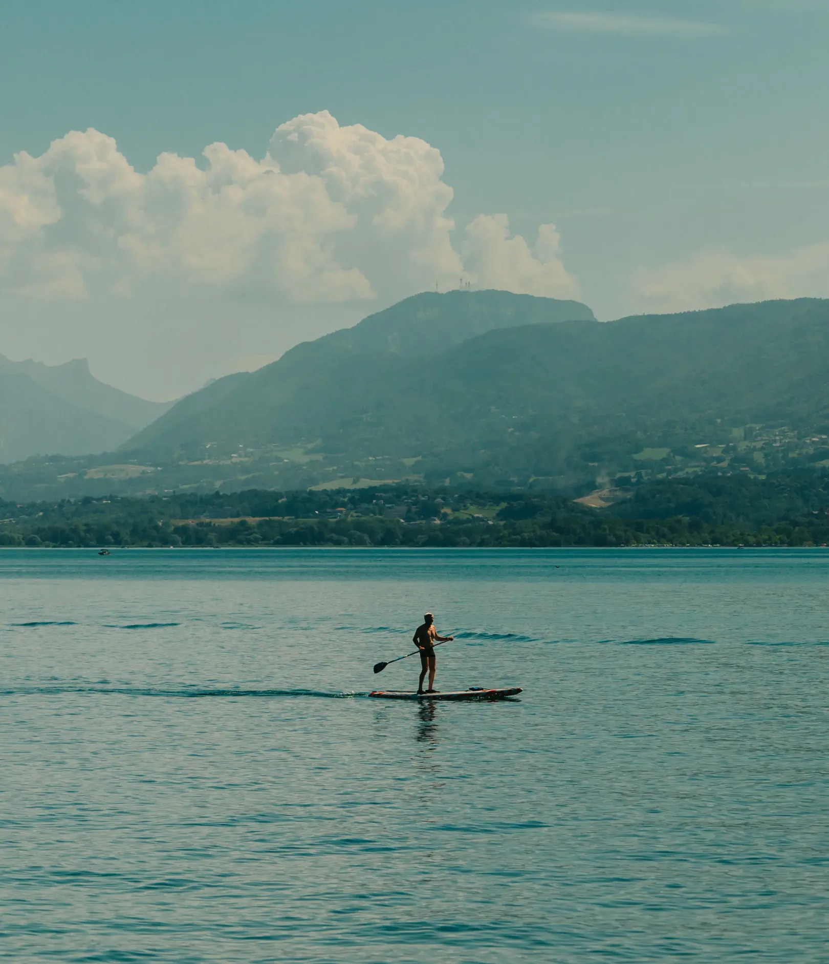 Une personne fait du paddle sur un lac avec des montagnes en arrière-plan