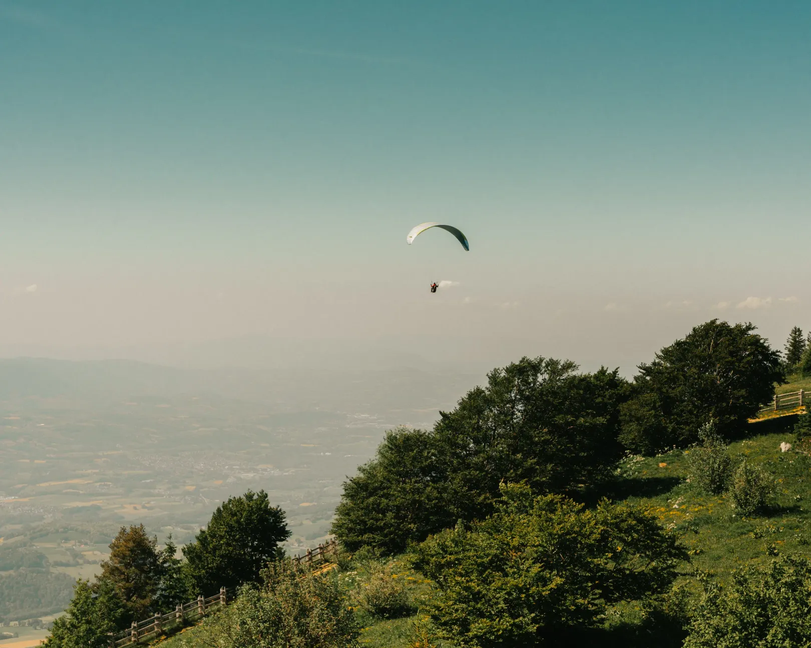 Un parapente vole au-dessus d'une colline boisée avec une vue sur une vallée en contrebas