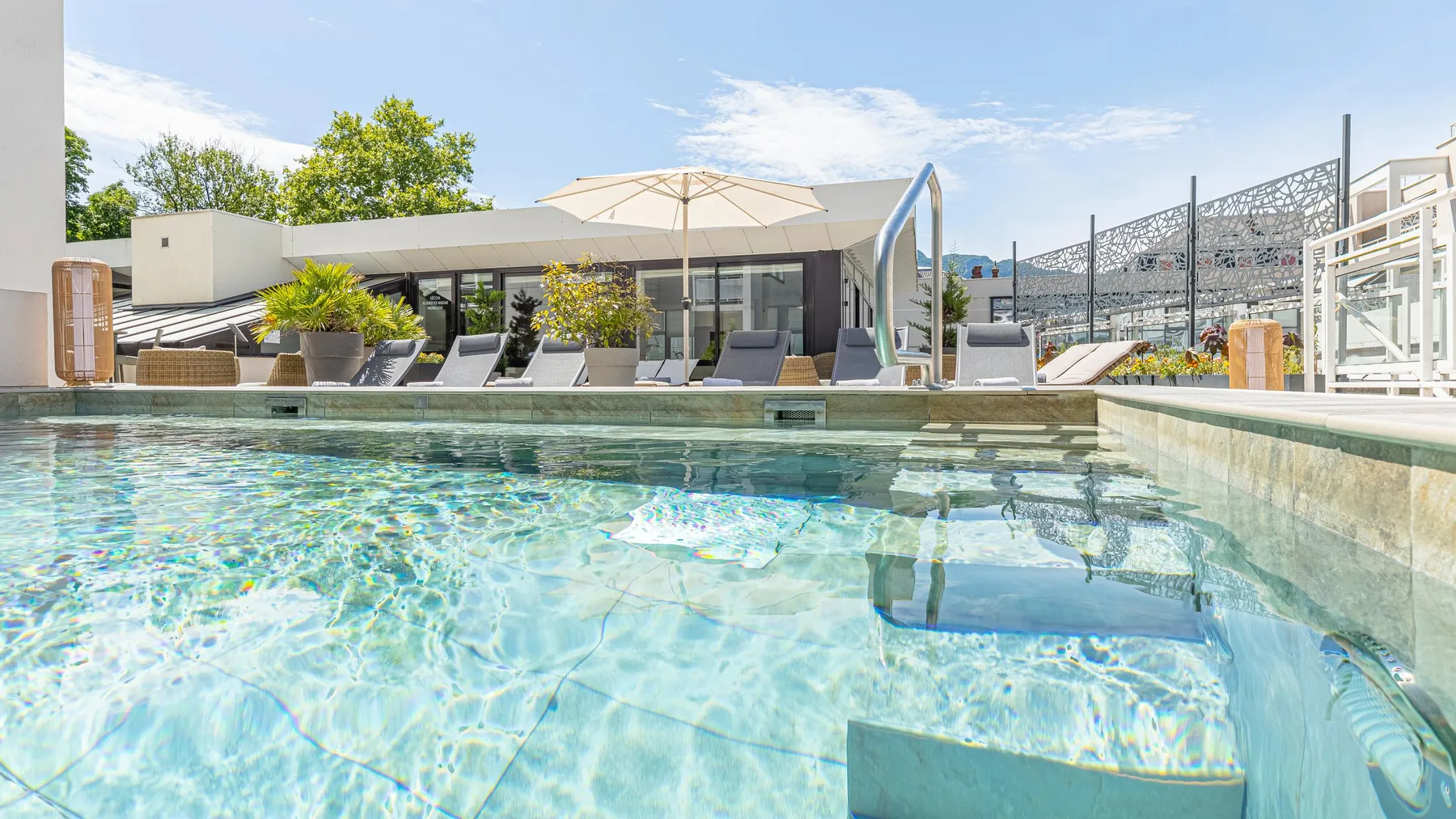 Pool with a view of a terrace equipped with sun loungers, umbrellas and greenery.