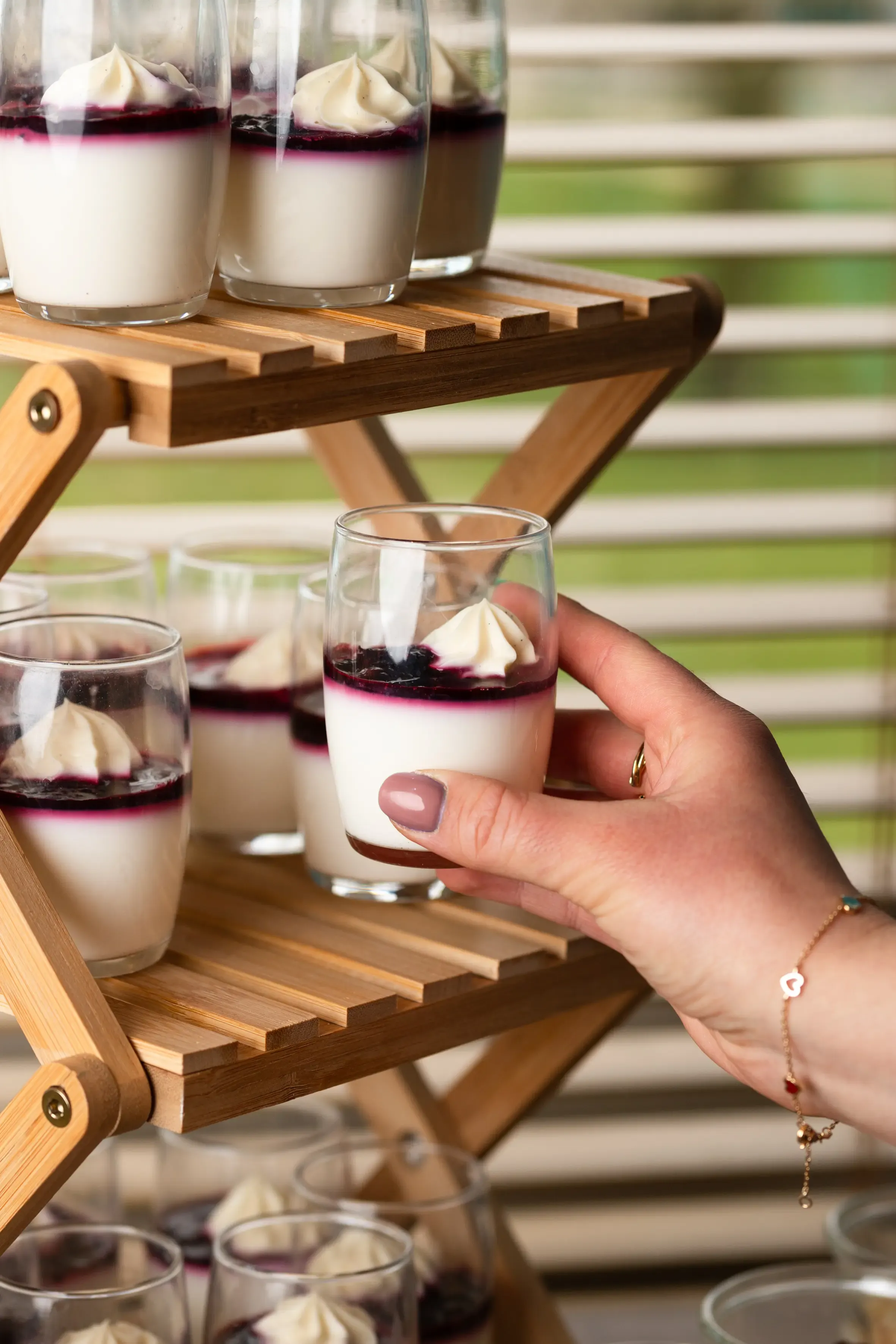 Une main tenant un verre de dessert à la vanille et aux baies, sur un plateau en bois avec d'autres verres similaires