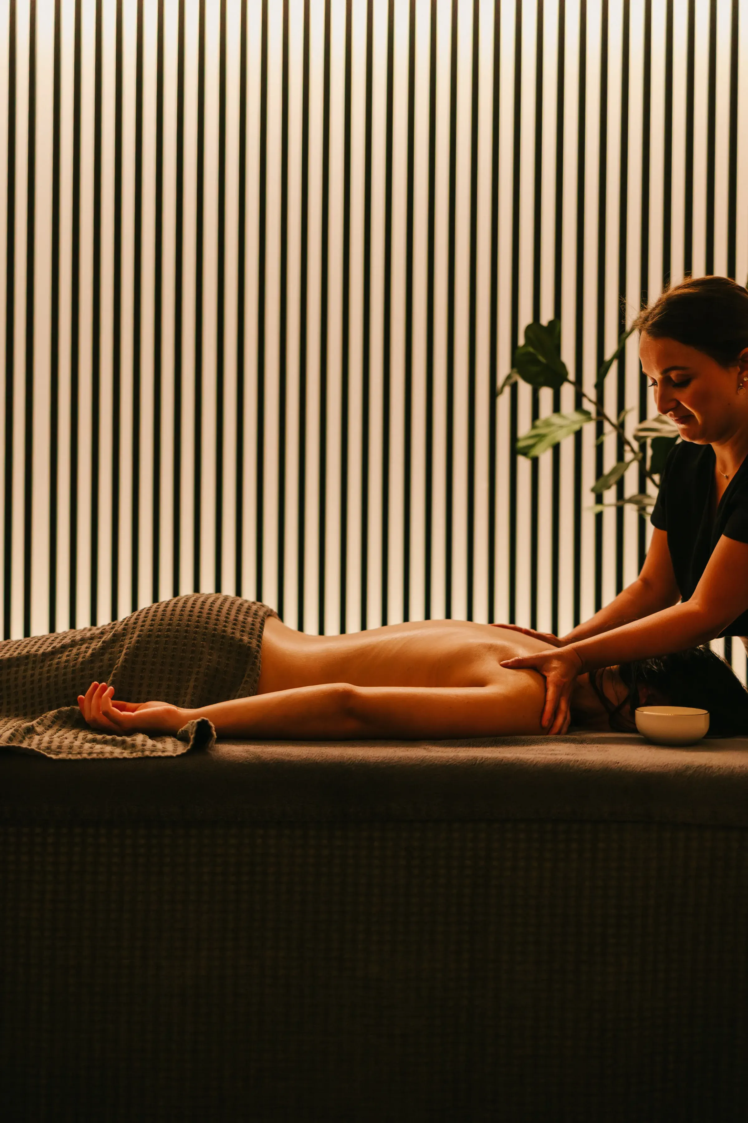 Une personne reçoit un massage sur une table dans une pièce aux murs à rayures verticales