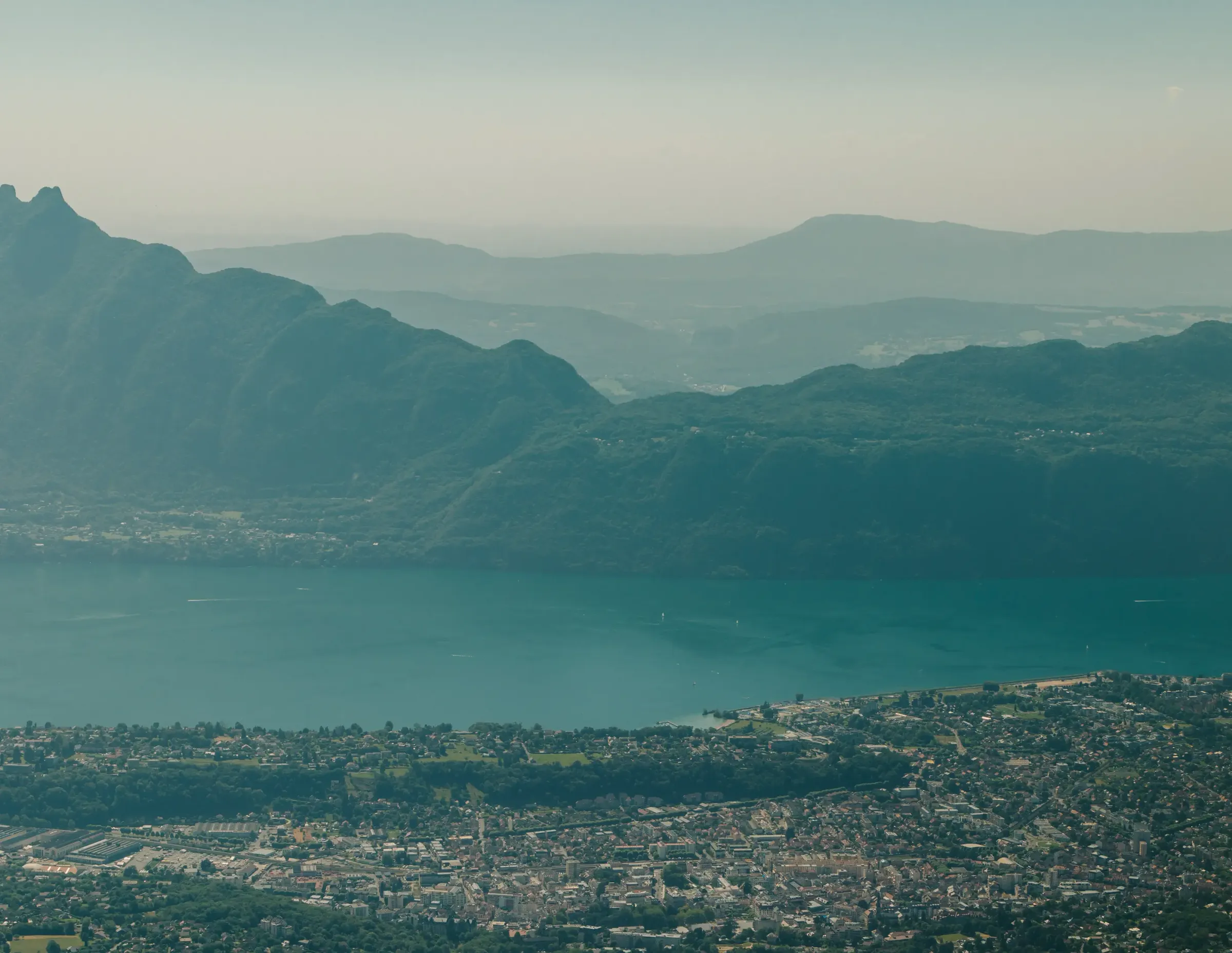Ville bordée par un lac entouré de montagnes avec des reliefs variés et une végétation dense