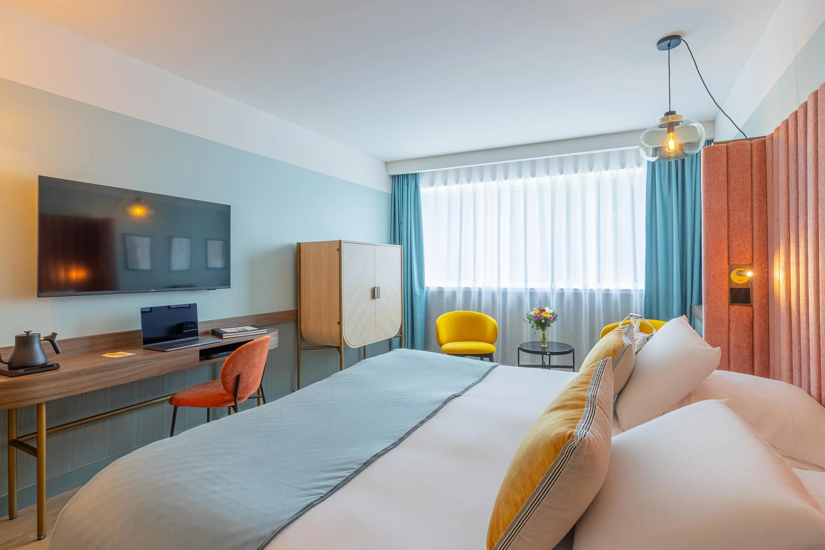 Chambre d'hôtel avec un lit double, une télévision, un bureau, une chaise jaune et une fenêtre avec des rideaux