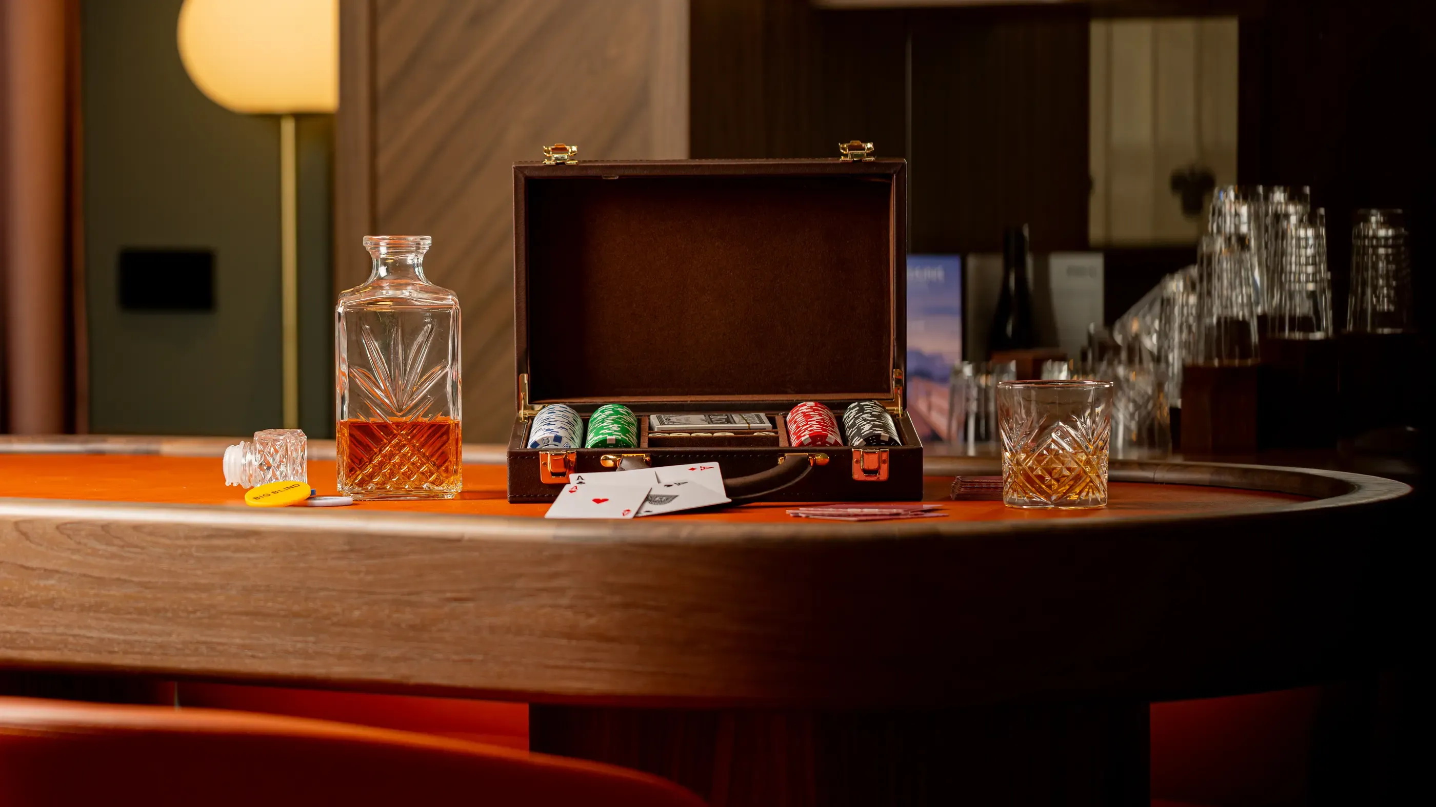 Une table avec un coffret de poker ouvert, des jetons, des cartes, un verre et une bouteille de whisky