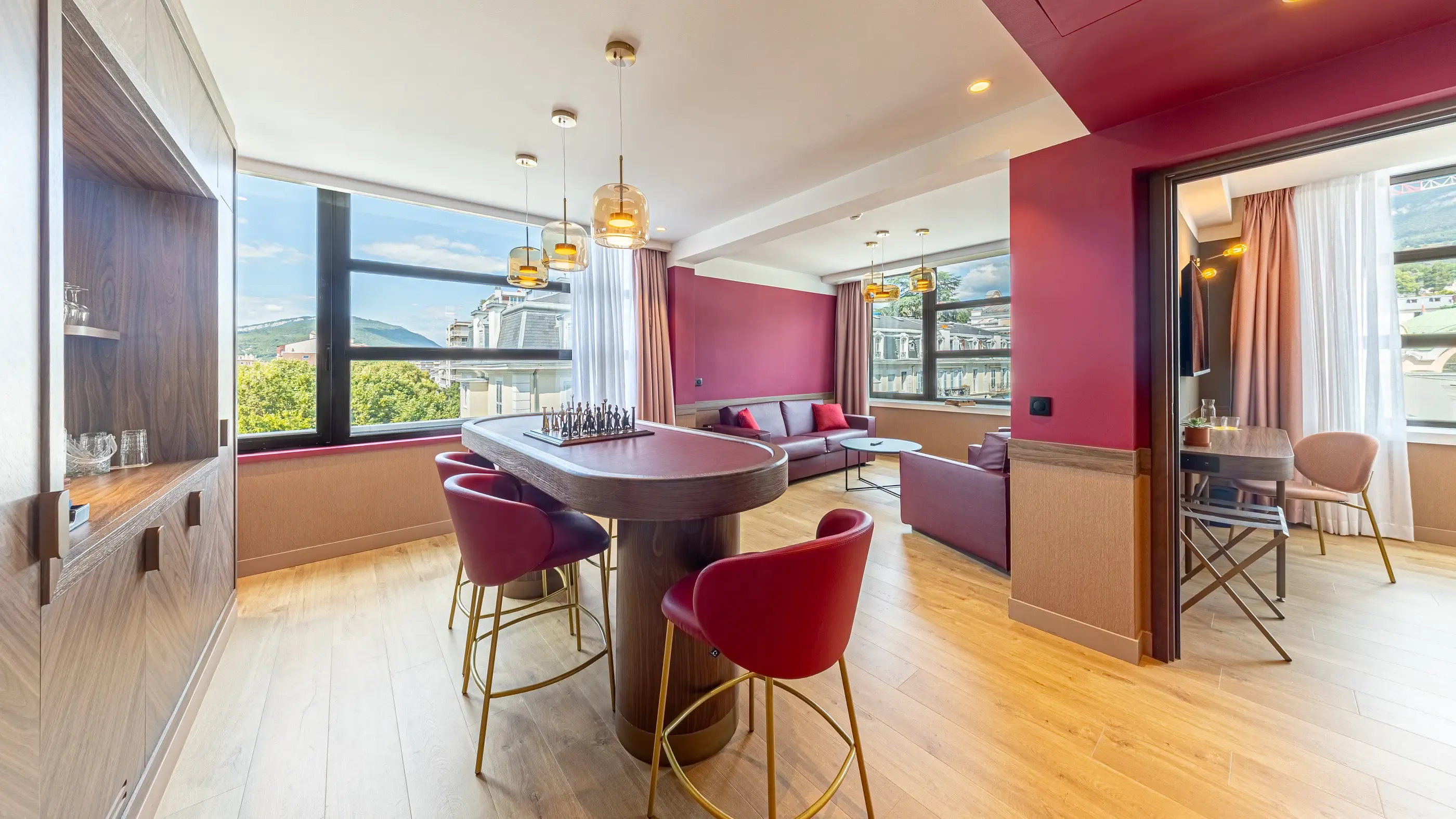 Salon moderne avec table ovale, chaises rouges, canapé gris et vue panoramique sur une ville