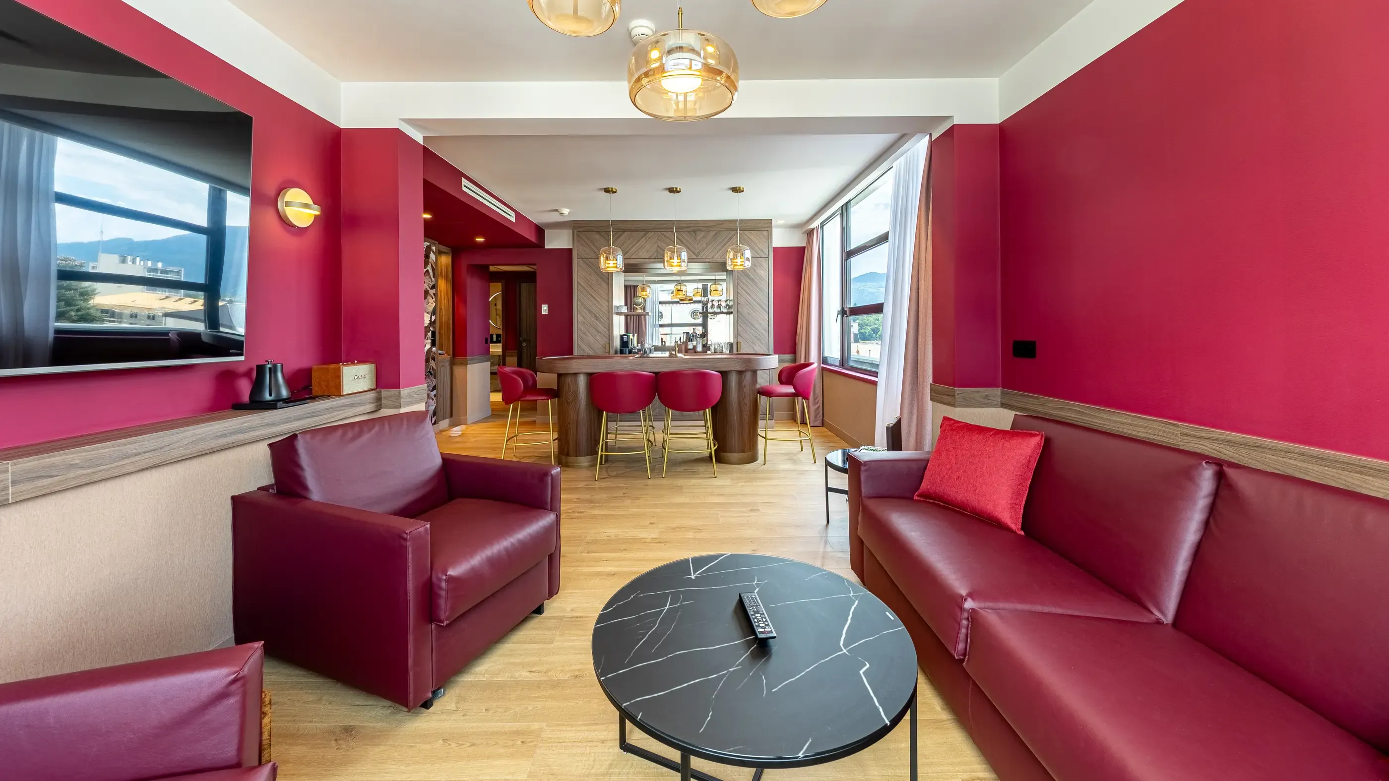 Salon avec canapés et fauteuils en cuir rouge, table basse noire, bar avec tabourets et vue panoramique