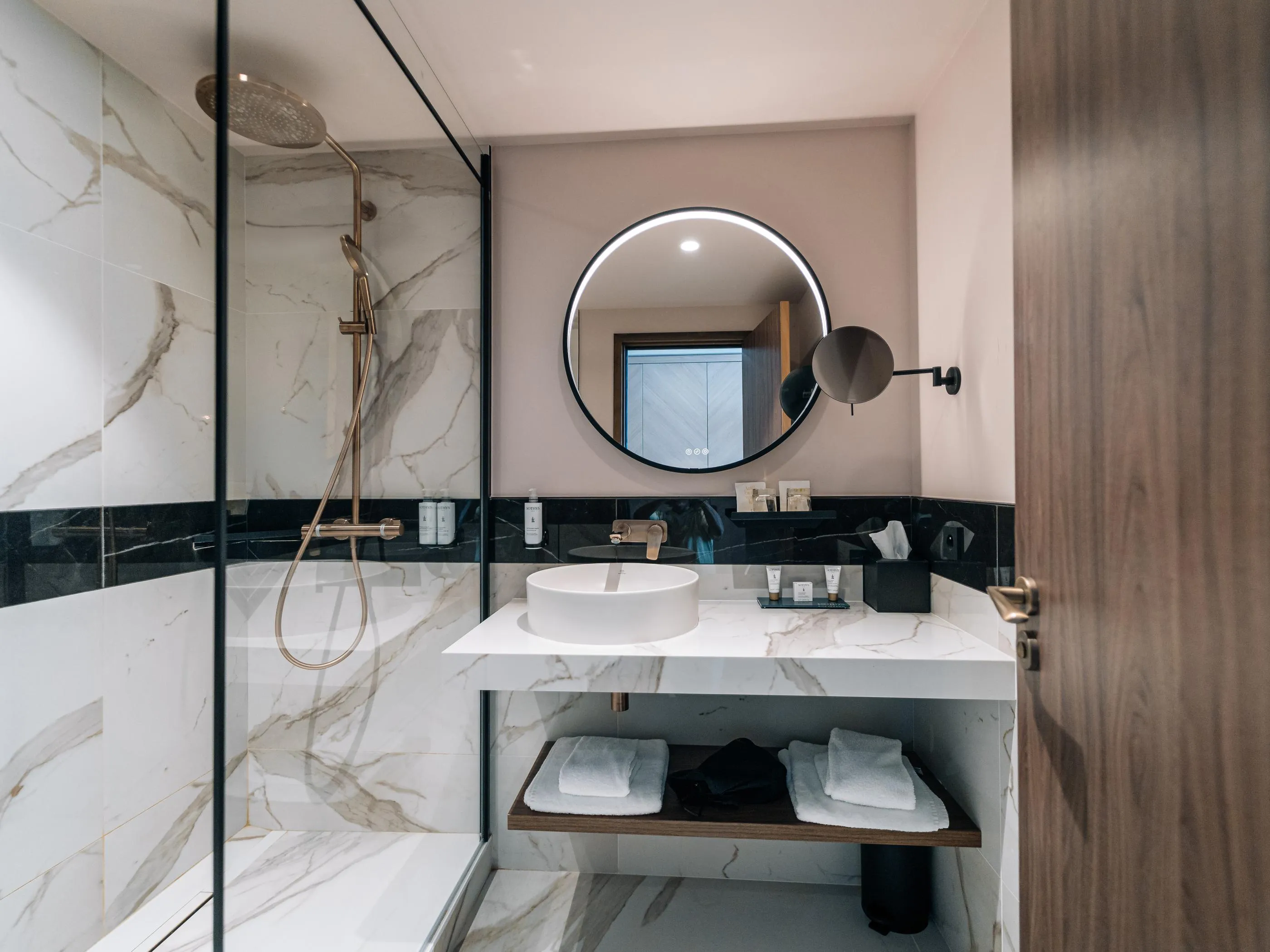 Salle de bain moderne avec douche en marbre, lavabo blanc et miroir rond éclairé