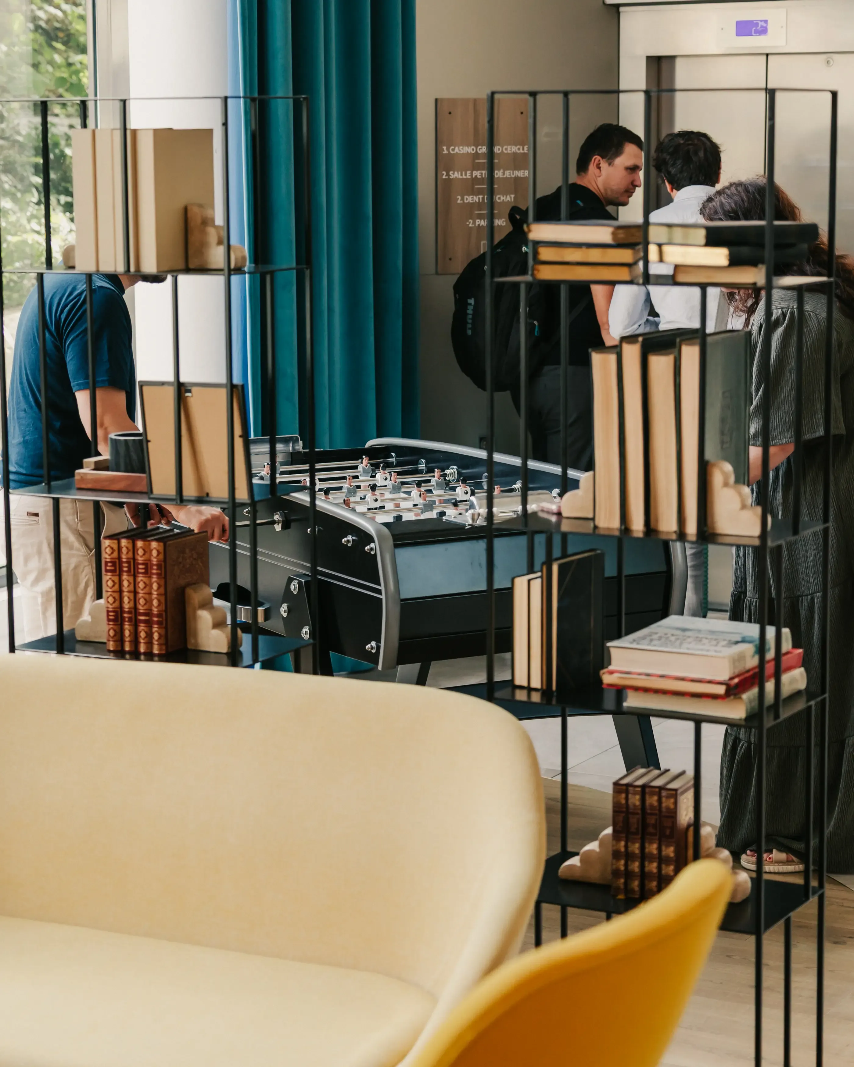 Des personnes jouent à un baby-foot dans un espace intérieur avec des étagères remplies de livres et des canapés