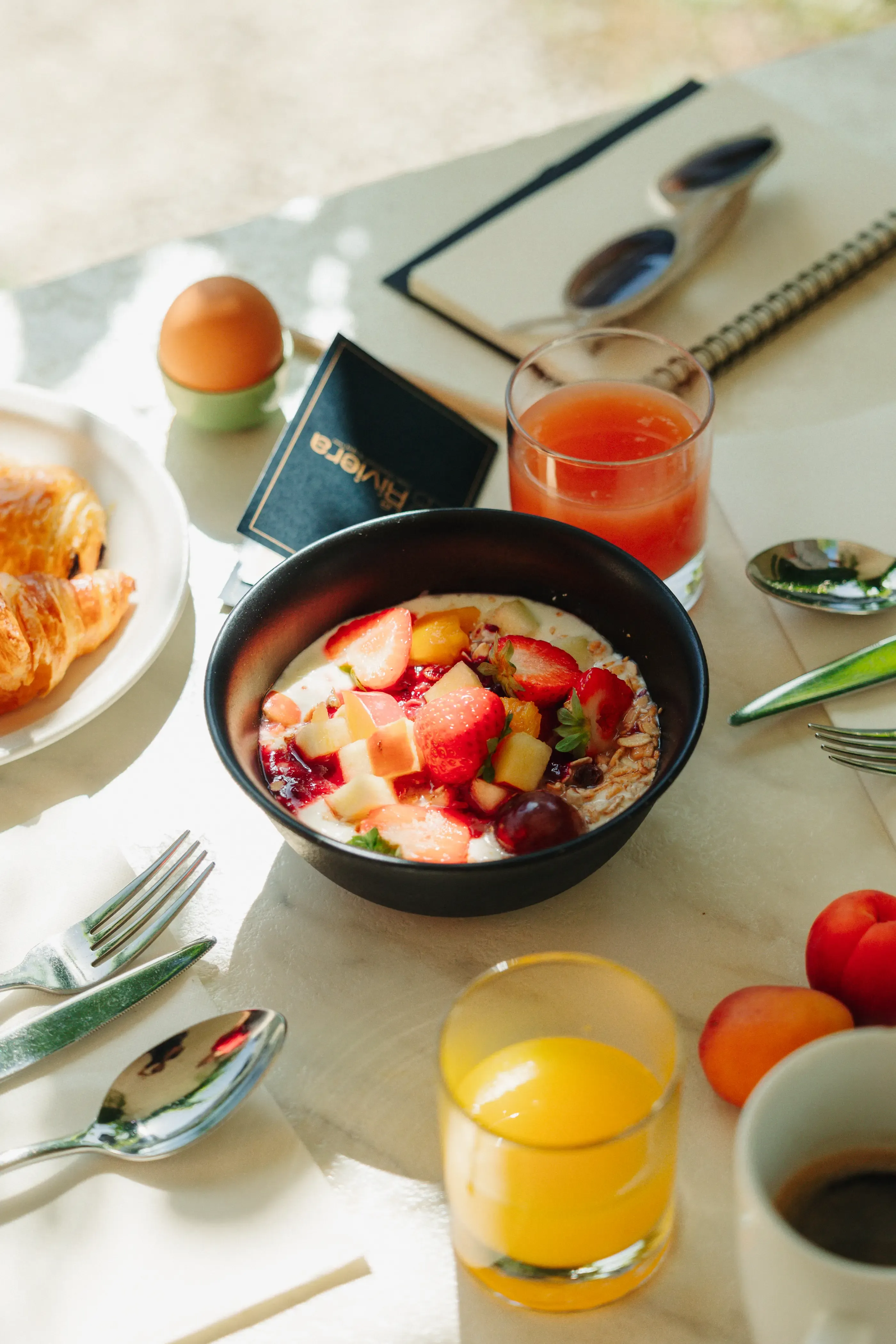 Un bol de porridge aux fruits frais, des croissants, des verres de jus, des couverts et des œufs sur une table