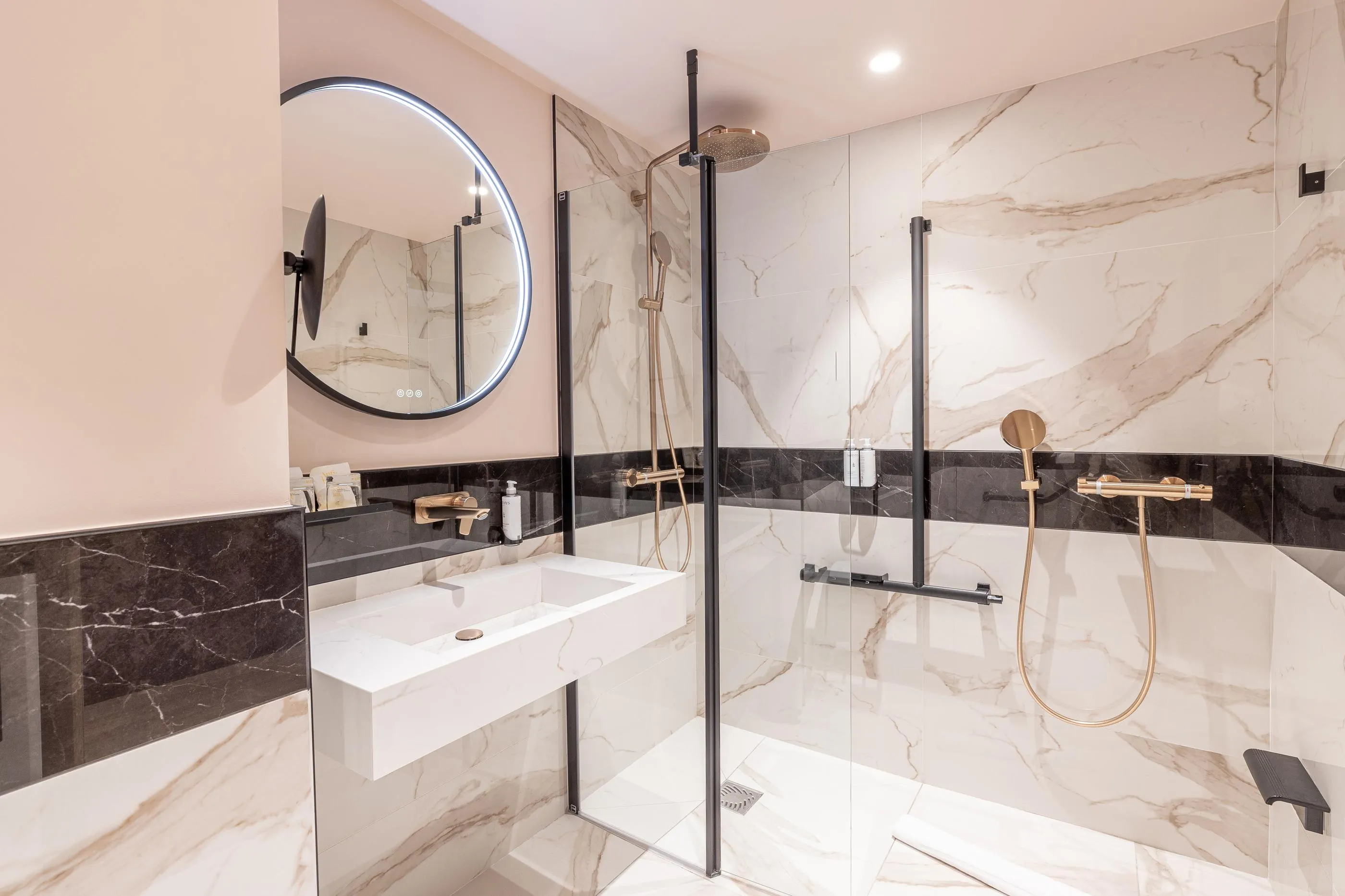 Salle de bain moderne avec douche à effet pluie, lavabo blanc et miroir rond encadré de noir