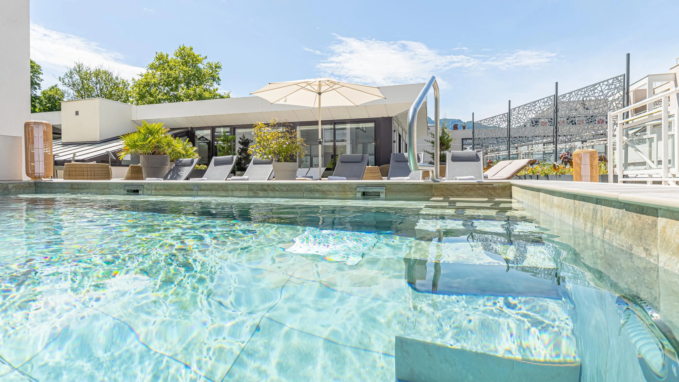 Pool with a view of a terrace equipped with sun loungers, umbrellas and greenery.