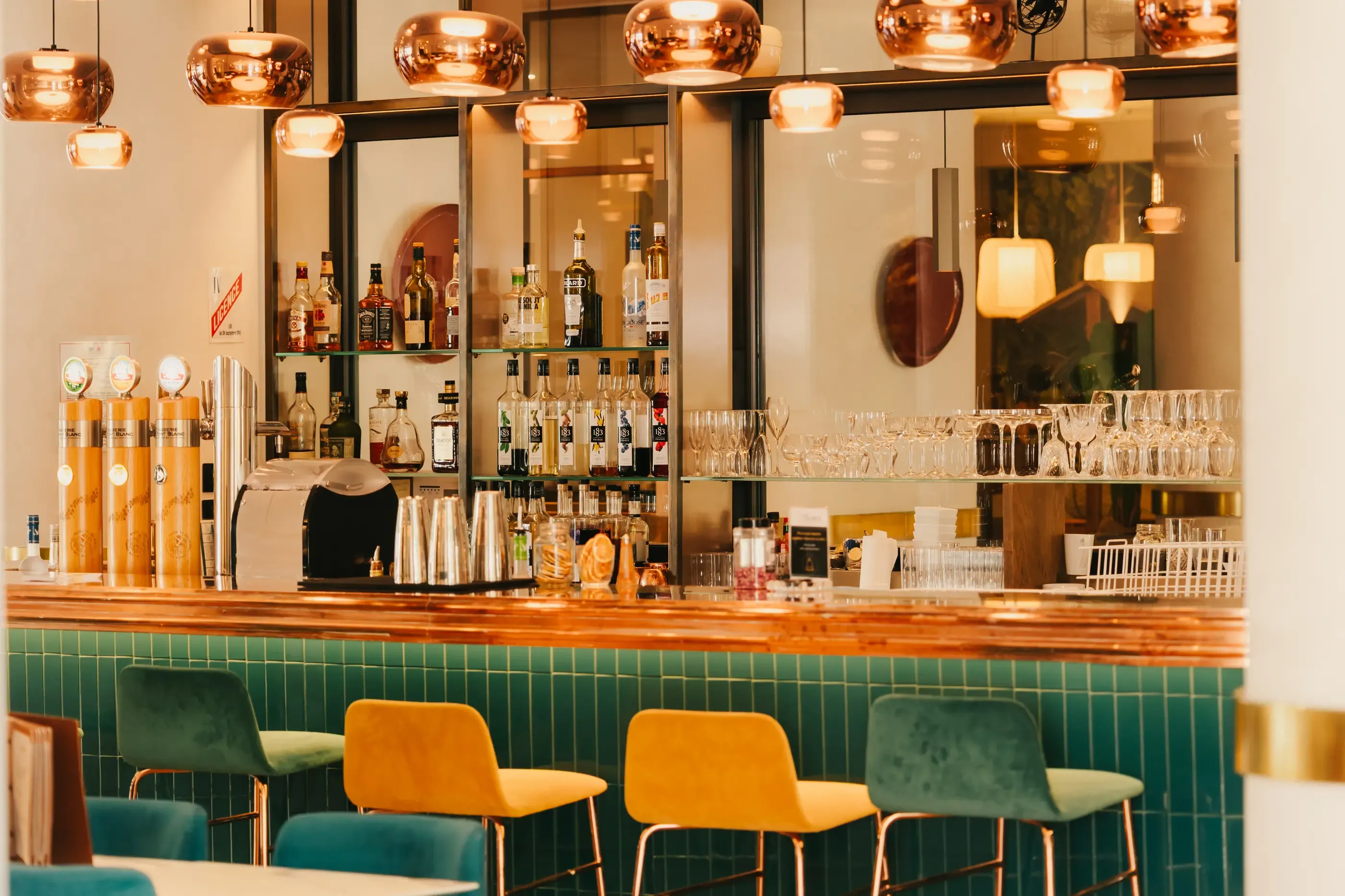 Un bar avec des étagères remplies de bouteilles d'alcool, des verres et des tabourets colorés devant un comptoir